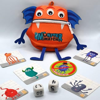 Monstermatch Verpackung ist ein oranges Monster mit blauen Armen und Beinen davor liegen Monsterkarten und zwei Würfel