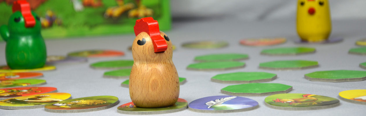 Zicke Zacke Hühnerkacke Gedächtnisspiel für Kinder ab 4 im Vordergrund holzfarbenes Huhn mit rotem Schnabel, es steht auf einem Laufplättchen