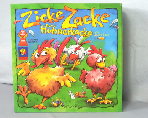 Spielschachtel Zicke Zacke Hühnerkacke grüne Schachtel mit drei Hühnern die auf einer Wiese laufen