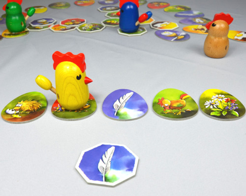 Zicke Zacke Hühnerkacke Plättchen aus dem Hühnerhof zeigt das Motiv Feder, das gelbe Huhn muss bei seinem nächsten Schritt auf das Feder-Wegplättchen treten. Der Spieler kann vorwärts laufen.